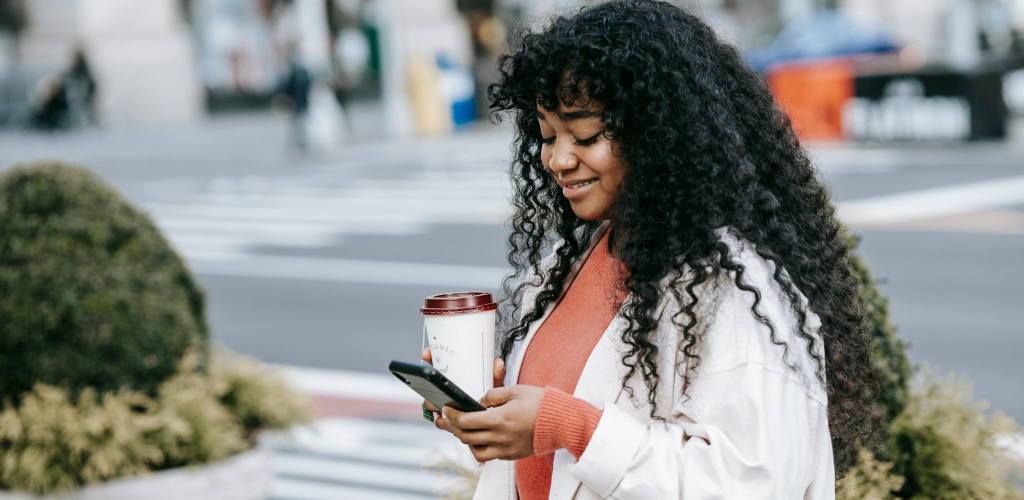 Woman completing her opportunity card application while walking and drinking coffee