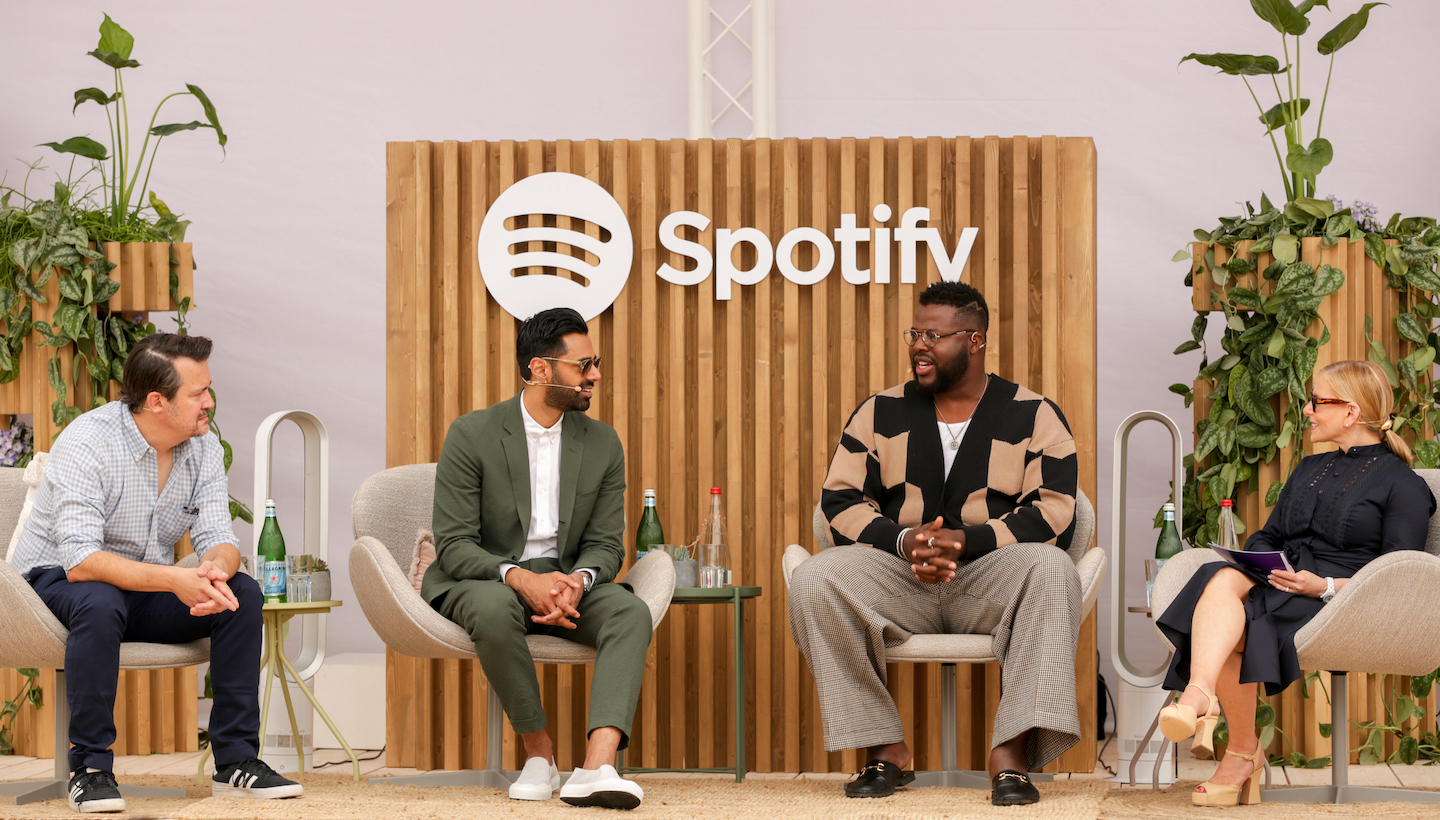 Peter Girardi, Hasan Minhaj, Winston Duke and Dawn Ostroff sit outside on a stage in front of a spotify logo. they are having a conversation.