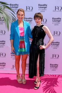 Dustee Jenkins and Maisie Williams post in front of a white backdrop on a pink carpet.