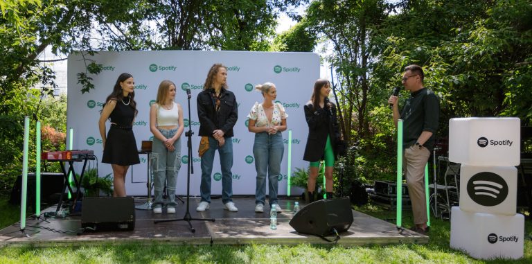 five singers standing on stage outside listening to a person speak