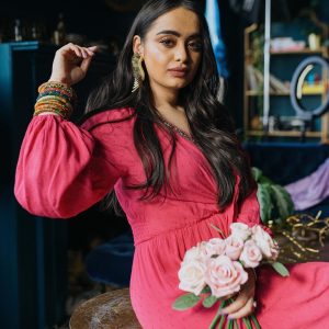 Trisha Sakhuja Walia posting in front of the camera wearing a pink dress and holding pink roses