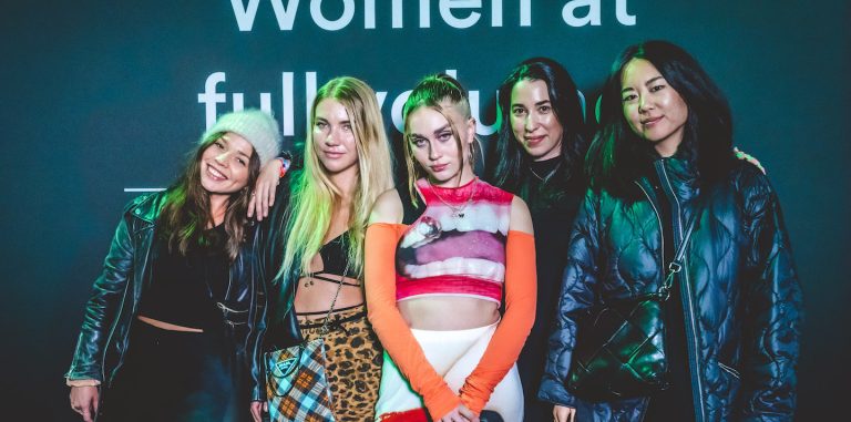 Five women posing in front of a camera at the music festival