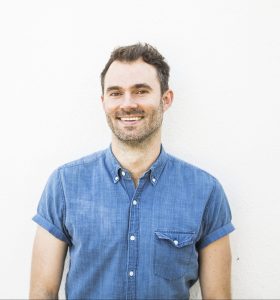 Rob Lowry posing looking directly at the camera and smiling. He is wearing a blue chambray shirt.