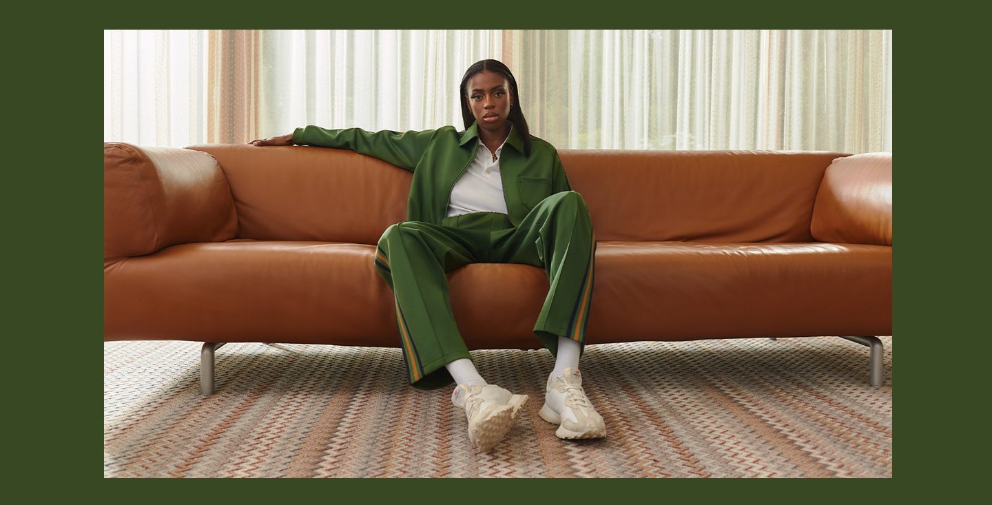 a photo of Cat Burns sitting on a brown leather couch, wearing a green tracksuit, and staring at the camera