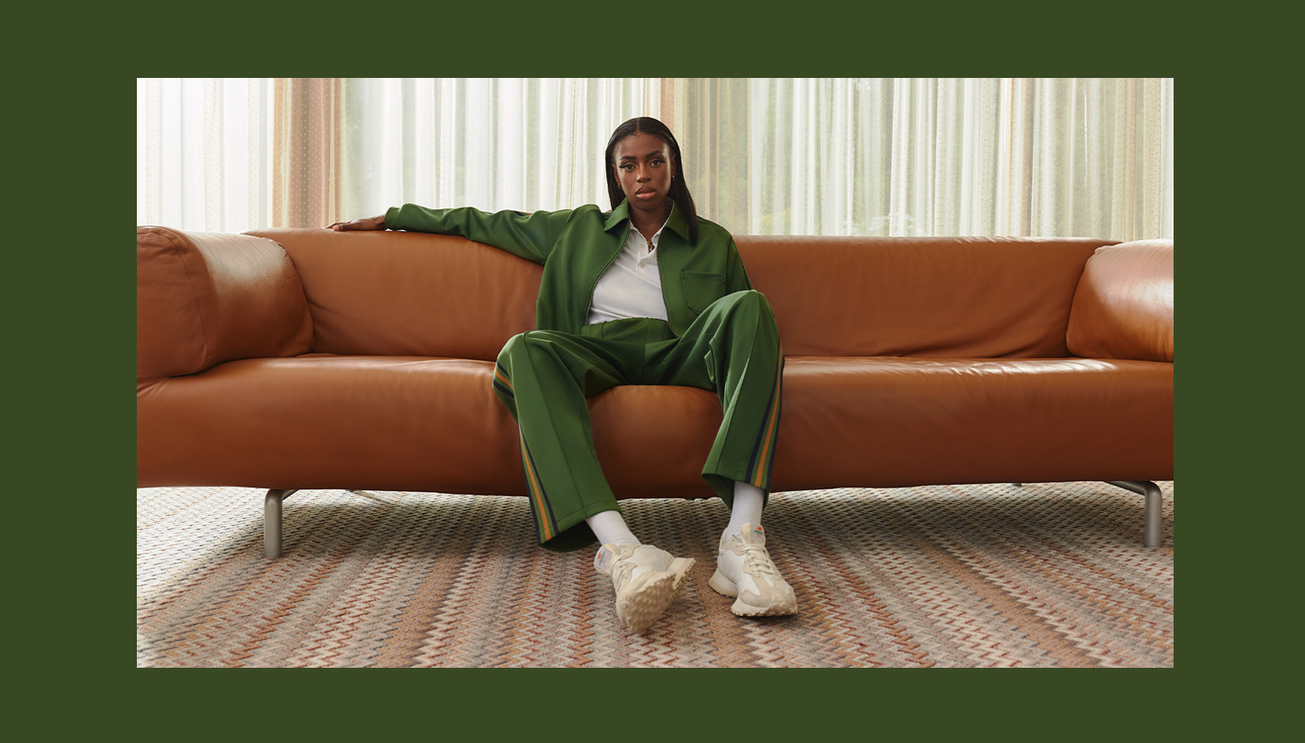 a photo of Cat Burns sitting on a brown leather couch, wearing a green tracksuit, and staring at the camera