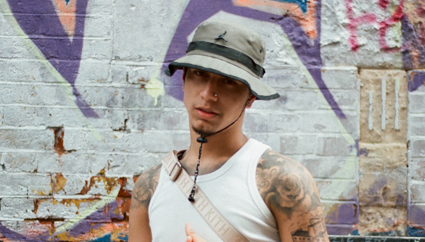 The artist Veigh poses in front of a wall covered in graffiti