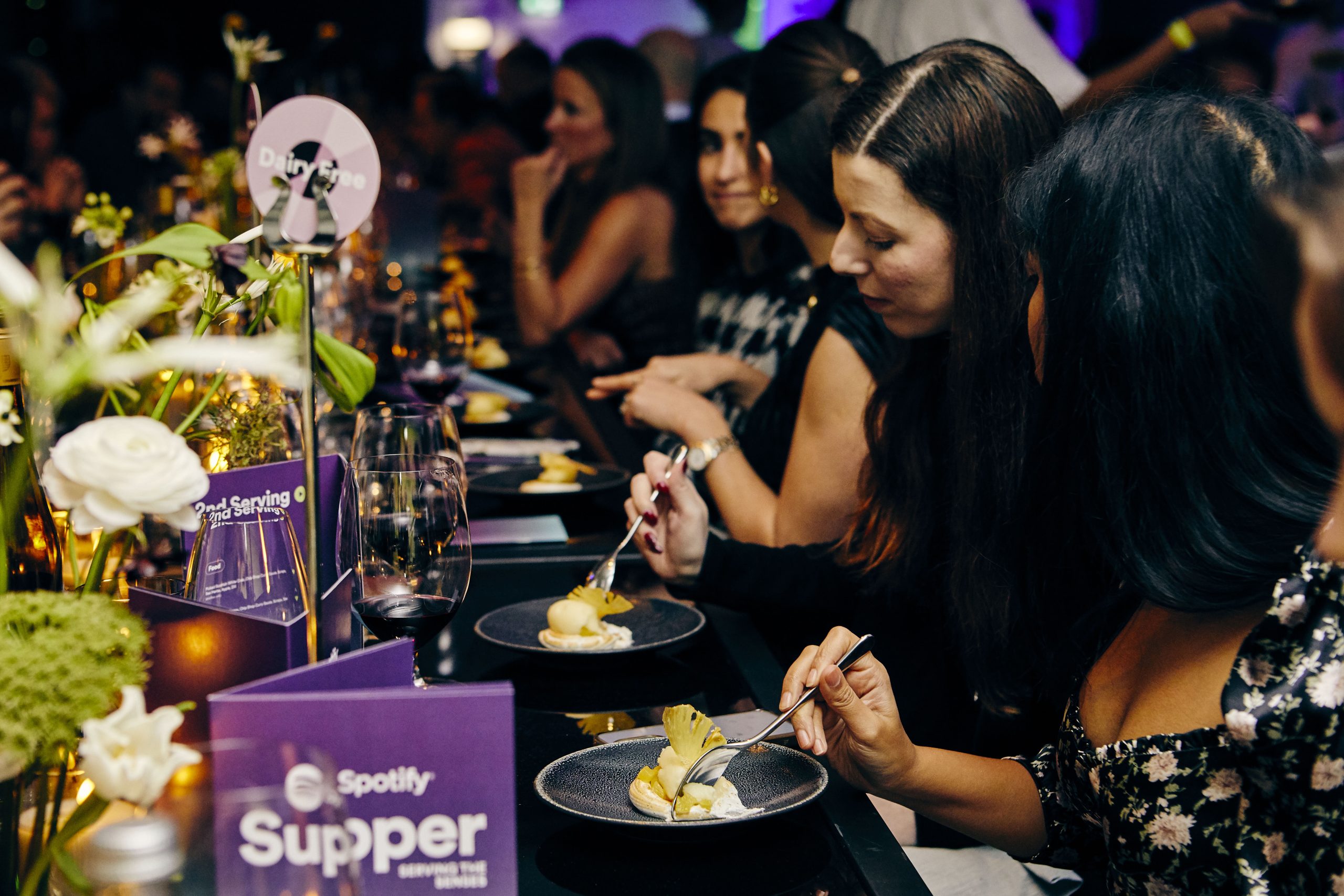 People sitting at a dinner table at a spotify supper eating food 