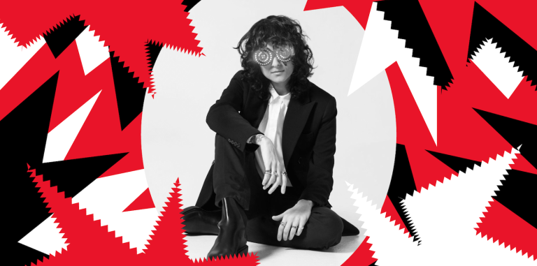 DJ Rezz sitting on the floor cross legged in a black and white suit. There are red, black, and white graphic elements bordering the picture