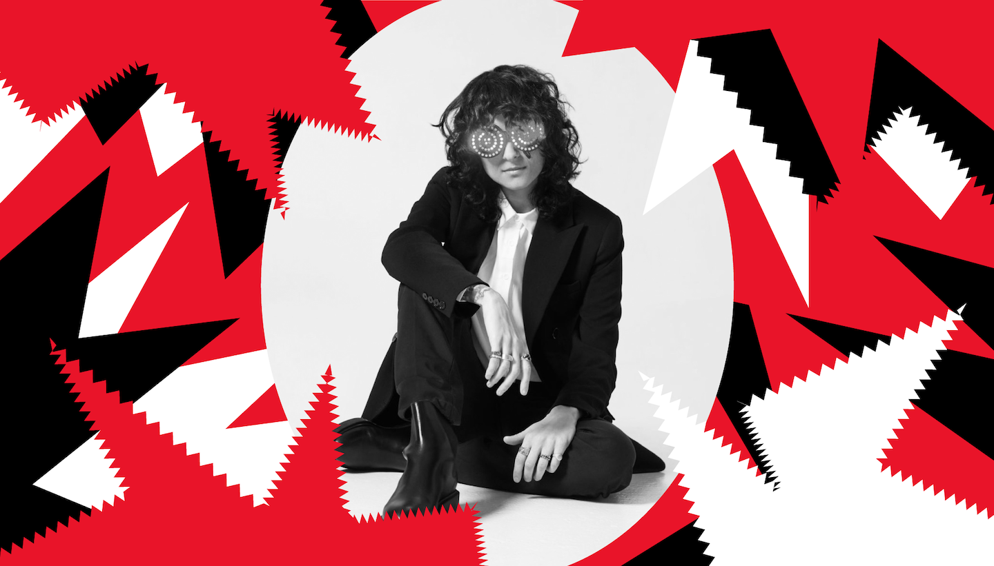 DJ Rezz sitting on the floor cross legged in a black and white suit. There are red, black, and white graphic elements bordering the picture