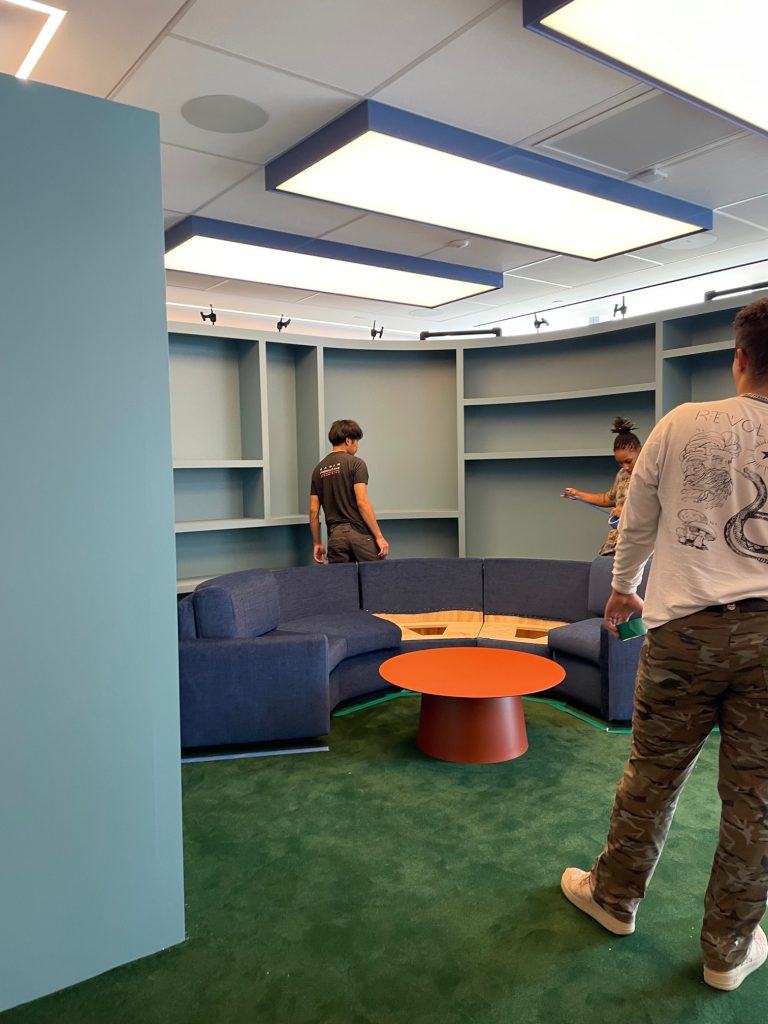 an office room with a blue couch and orange table, people arranging furniture