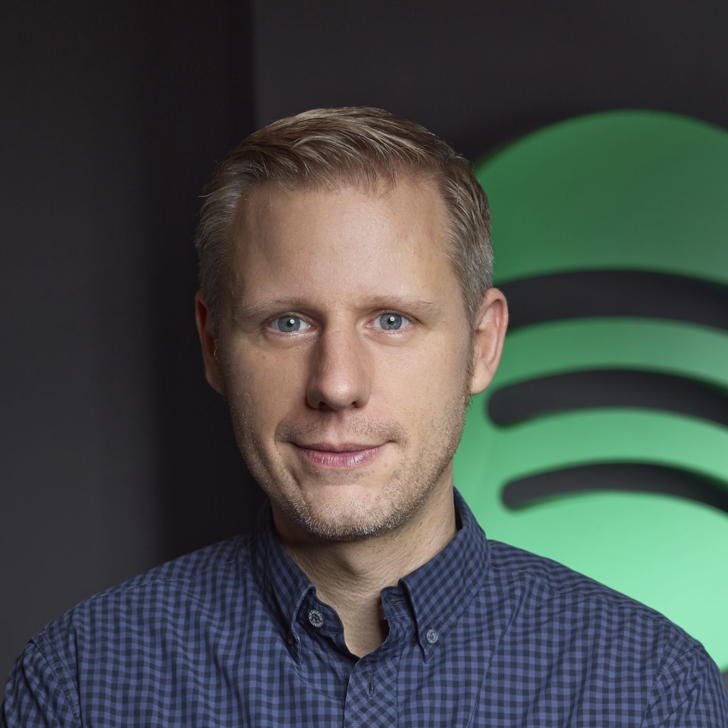 Michael Krause staring directly at camera, wearing blue button down against a background with the Spotify logo