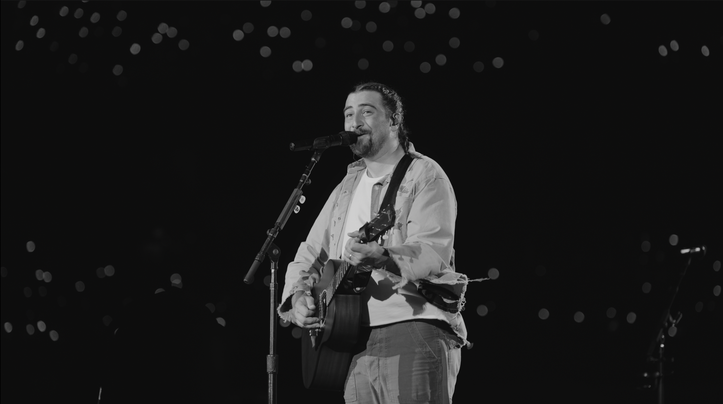 Noah Kahan appearing on stage holding a guitar and singing into a microphone