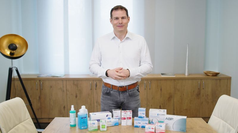 Sortiment PraxisPanda Ein Mann steht vor einem Tisch, der mit verschiedenen Medizinprodukten gefüllt ist.