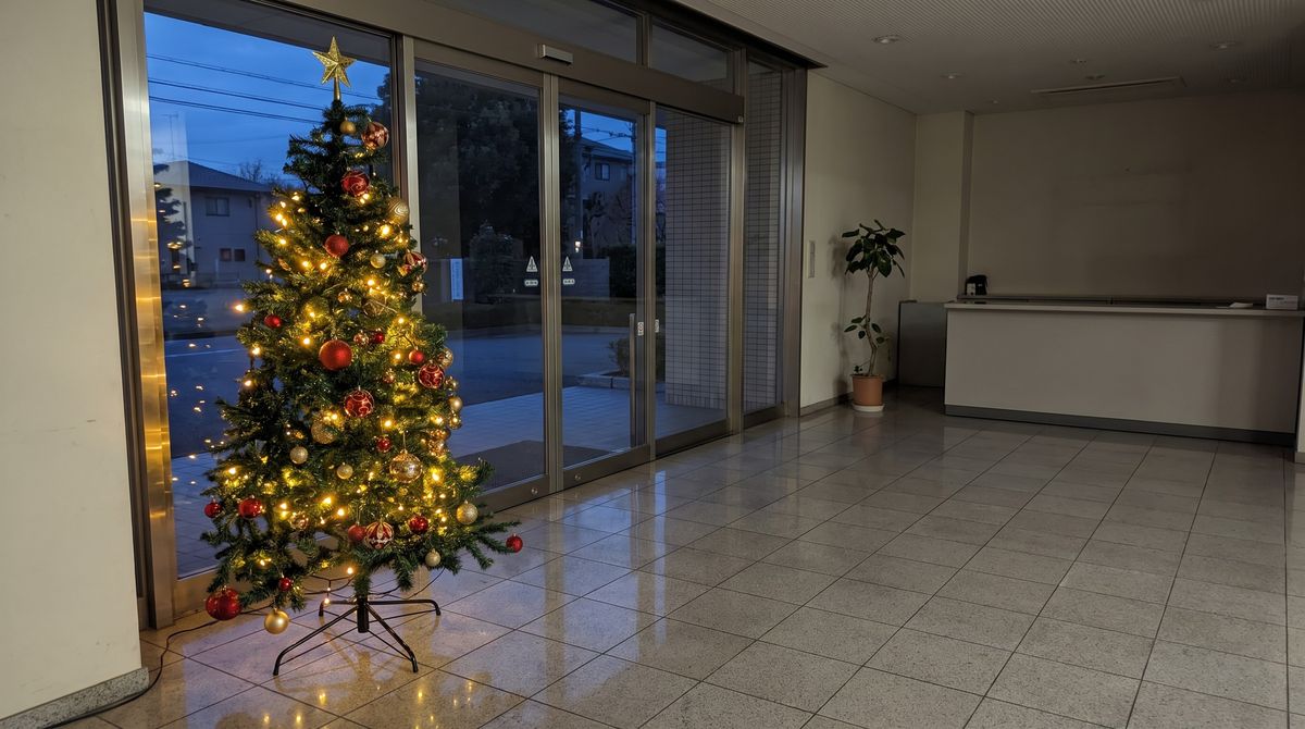 オフィスのエントランスのガラス戸の横に置いた180cmのクリスマスツリーセット。電球色のLEDライトとオーナメントボール、トップスターが付いている