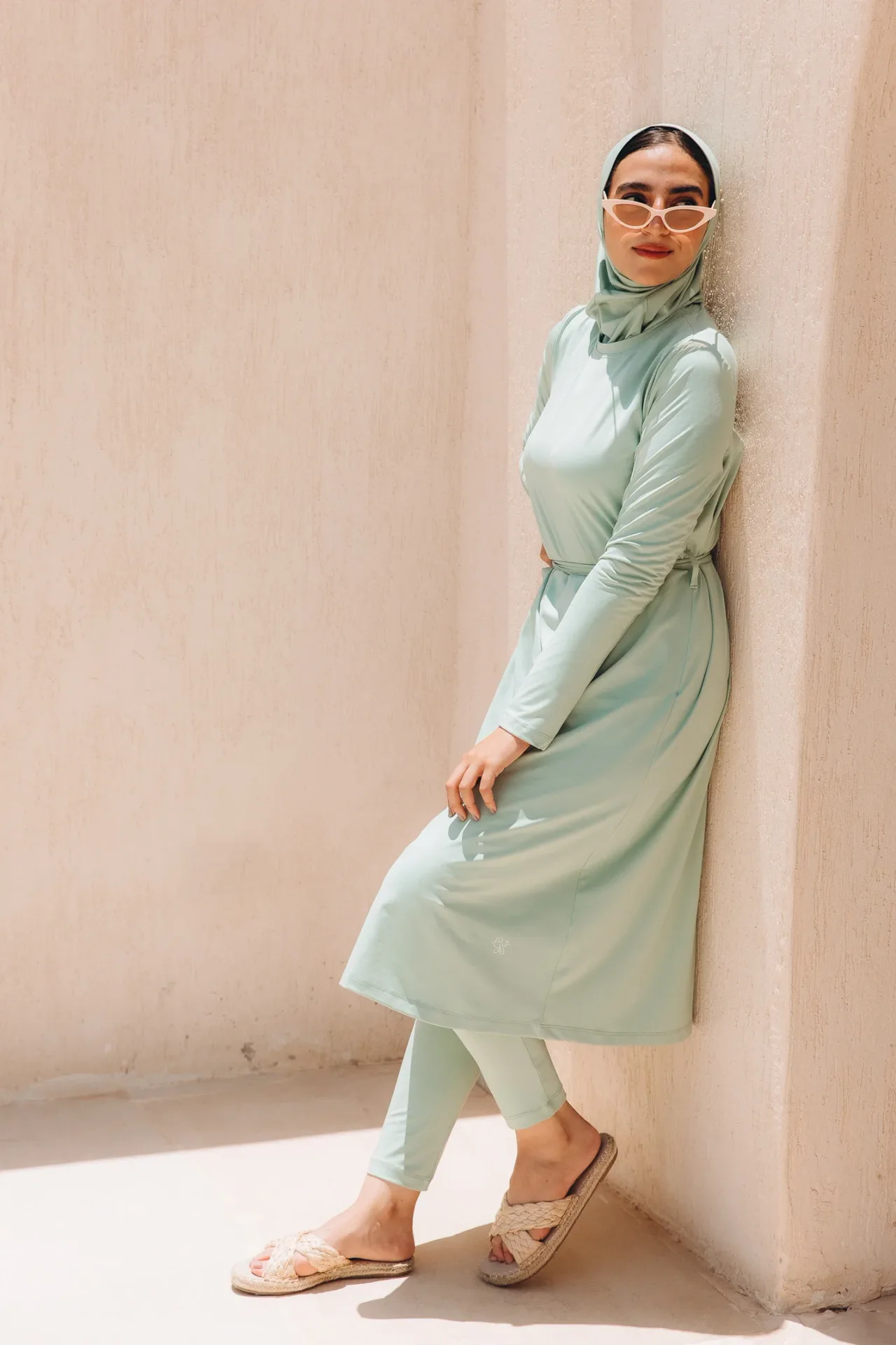 Monochrome mint outfit with a long-sleeve midi dress, matching cropped leggings and hijab, paired with beige braided slide sandals and white cat-eye sunglasses.