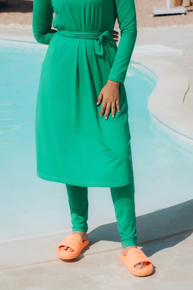 Emerald green long-sleeve tunic dress with self-tie waist worn over matching leggings, paired with orange padded slide sandals.