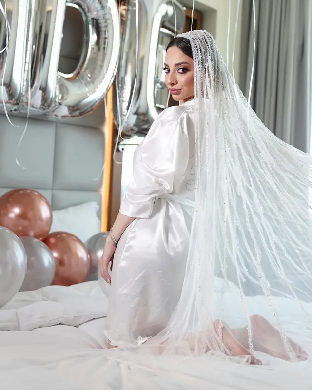 White satin knee-length robe with three-quarter sleeves paired with a long beaded veil and metallic balloons in the background