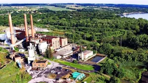 An aerial photo of a power plant, with trees and a lake in the background