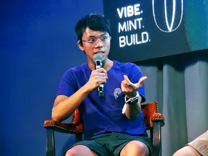 Ian Macalinao sitting in a folding chair and speaking into a microphone, gesturing at someone out of frame