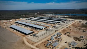 An aerial photo of large warehouse-style buildings, electricity infrastructure, and shipping containers on a large dirt plot