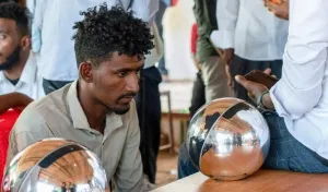 A man sits staring into a gleaming silver sphere