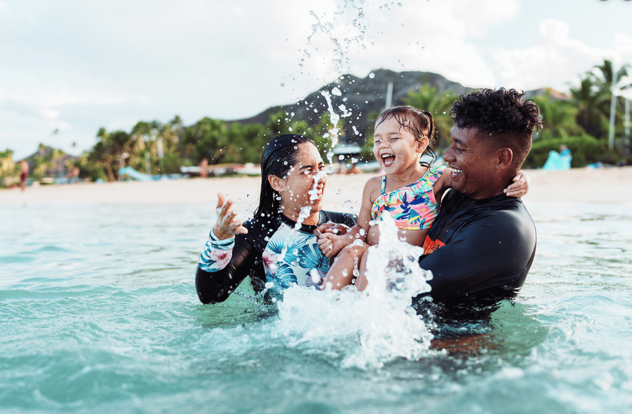 Happy family with young child playing in the ocean at an all inclusive beach resort