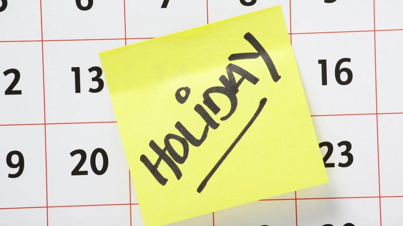 A sticky note with ‘holiday’ written on it is pasted on a calendar as a reminder for school holidays.