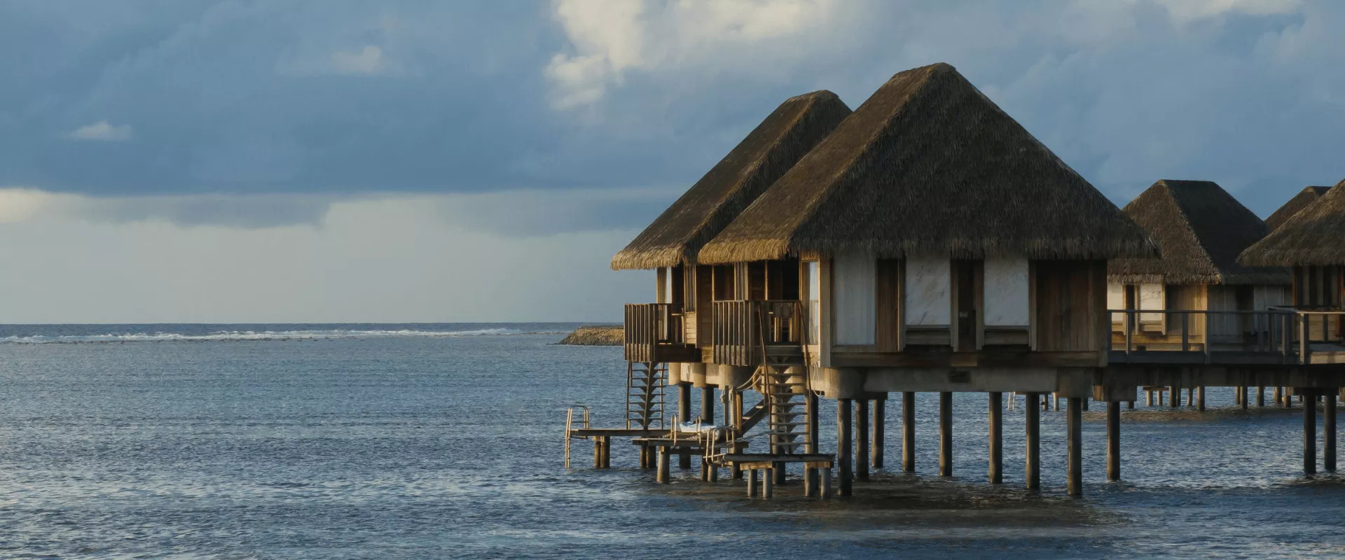 Water villas at Club Med Kani overlooking the ocean at sunset, with calm turquoise lagoon surrounding the resort.