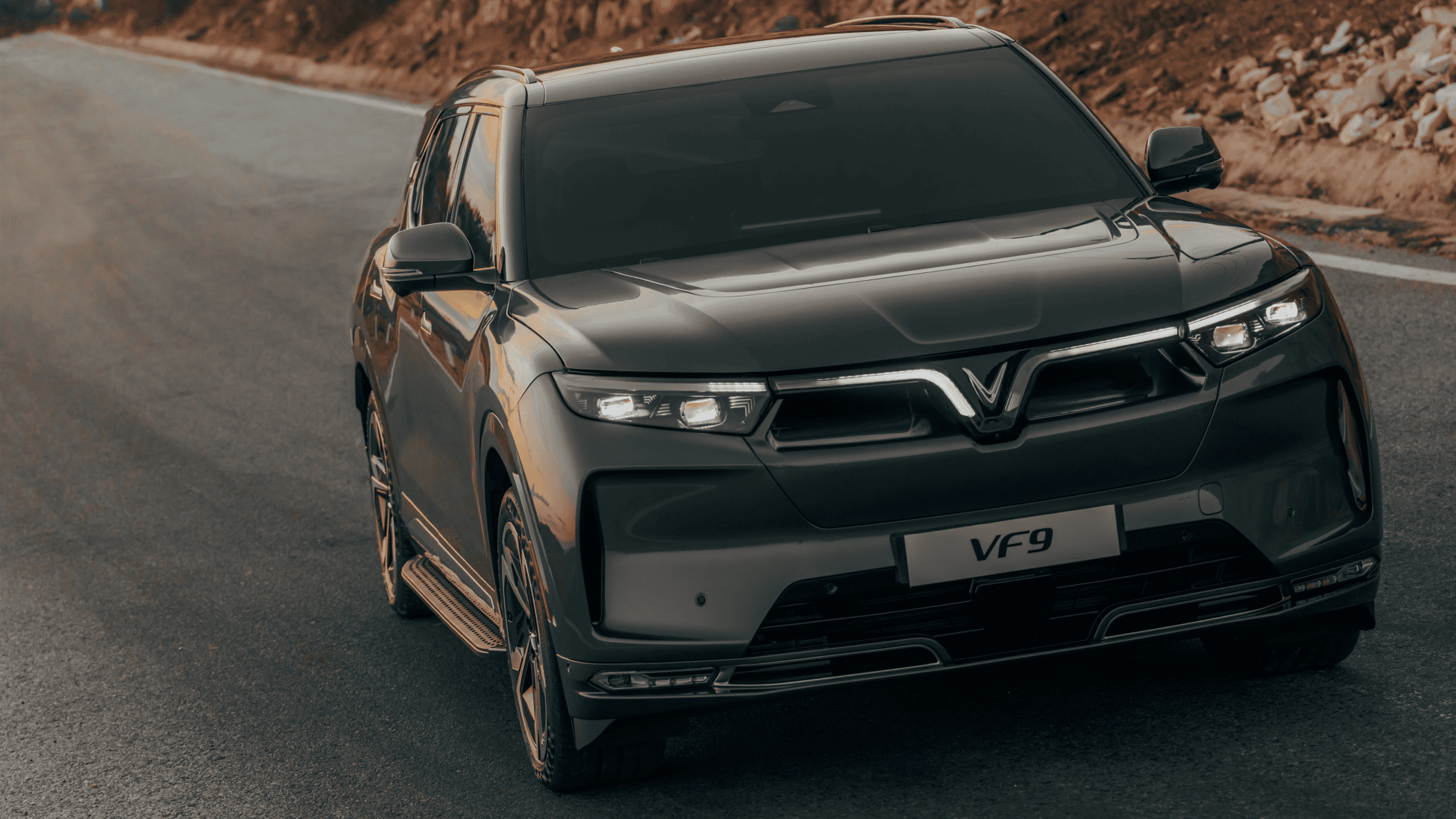 The VinFast VF 9, a luxury electric SUV, is seen driving down the road along rocky terrain.