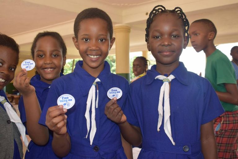 Girl Guides in blue uniform and white scarves holding up their Free Being Me badges