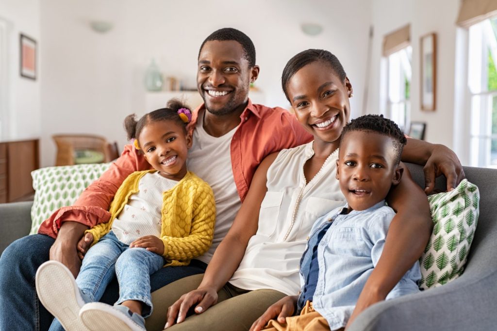 Portrait of happy mature couple with son and daughter relaxing on sofa at home. Middle aged black woman with husband and children smiling and looking at camera. Beautiful mid african american family.