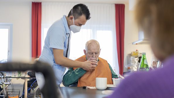 In this photo illustration a caregiver helps man to drink in nursing home in Heidelberg, Germany, on March 30, 2022. A new study suggests talking therapies can be very helpful for Alzhiemer's patients. GRABOWSKY/GETTY IMAGES  