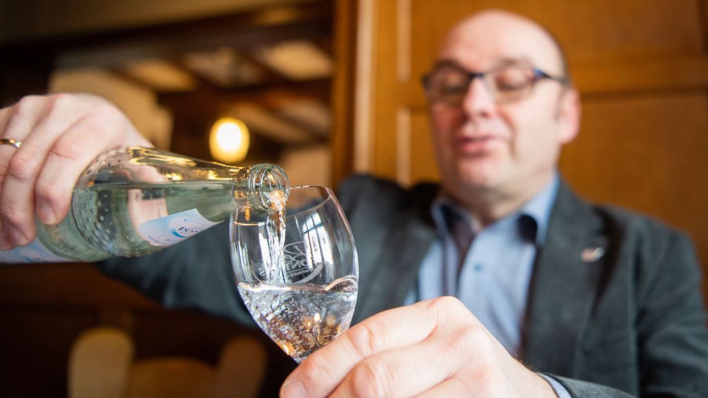 A man pours mineral water from a bottle into a glass. The 8x8 rules suggest to drink 8 glass of water daily. TOM WELLER/PICTURE ALLIANCE VIA GETTYIMAGES