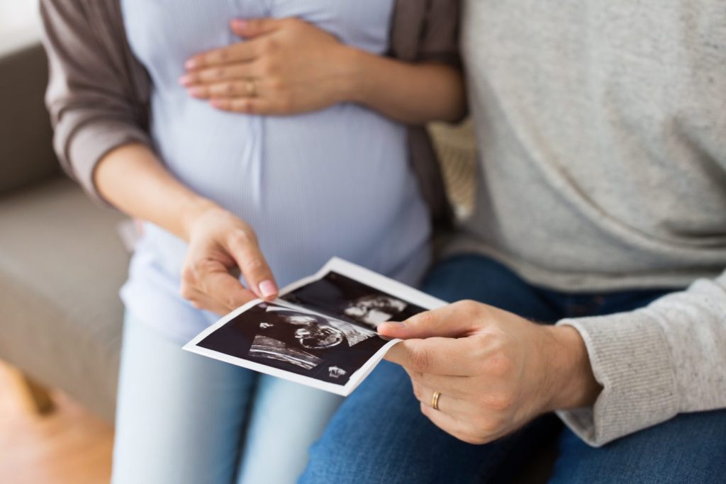 pregnancy, family and people concept - close up of man with his pregnant wife looking at baby ultrasound images at home