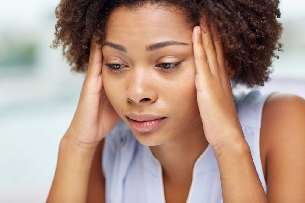 A woman holding her head looking like she is about to cry. 56 percent of women feel the pain they experience is ignored or dismissed. GROUND PICTURE/ VIA SHUTTERSTOCK