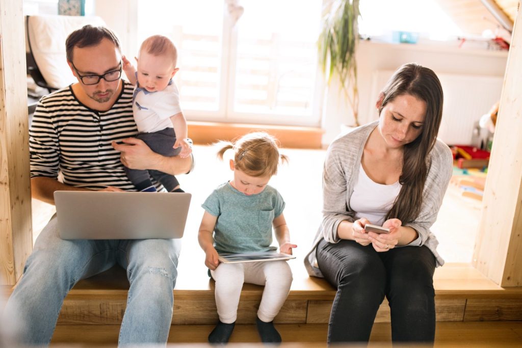 Young parents with little children and gadgets at home.