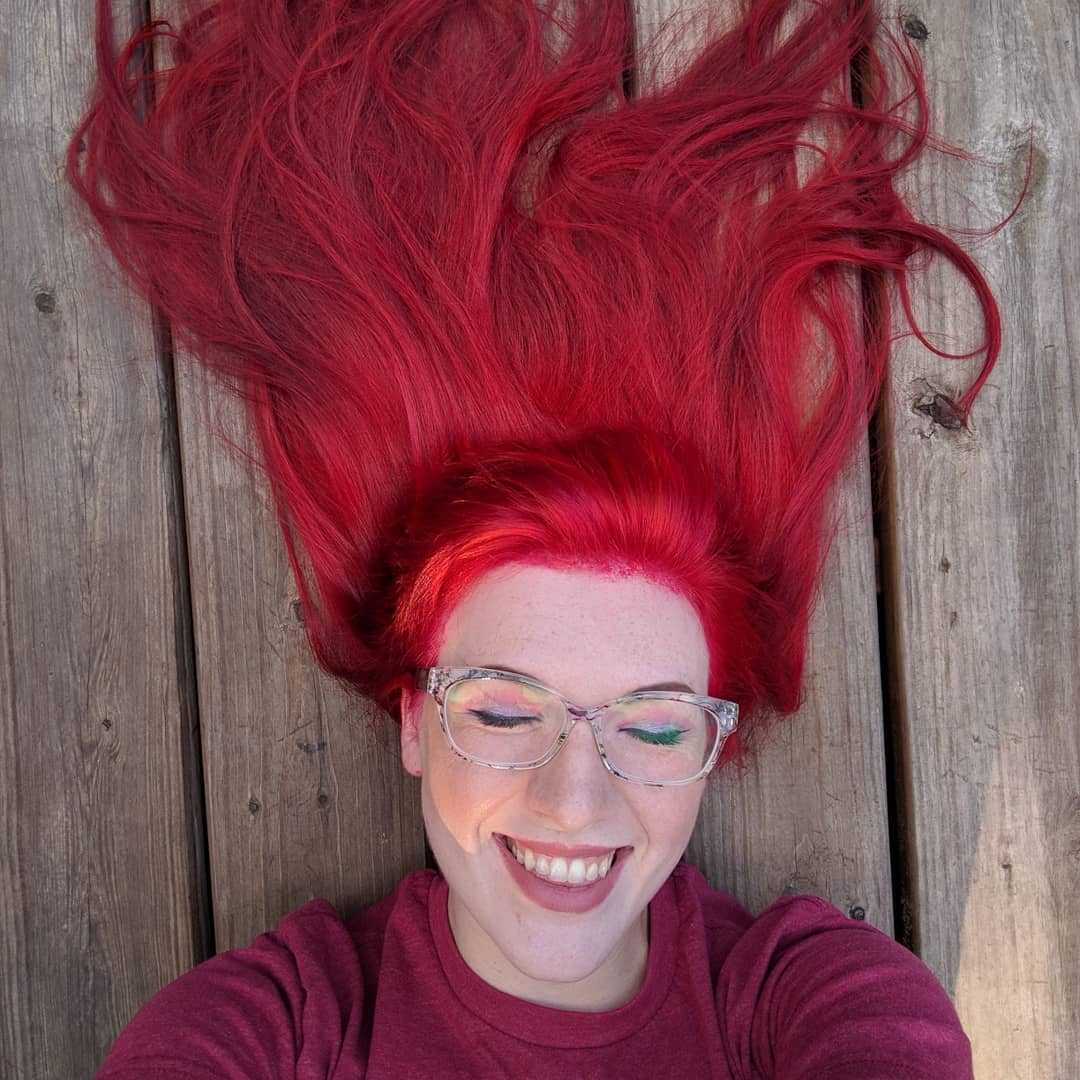 Caucasian with flowing red hair, glasses and a big smile
