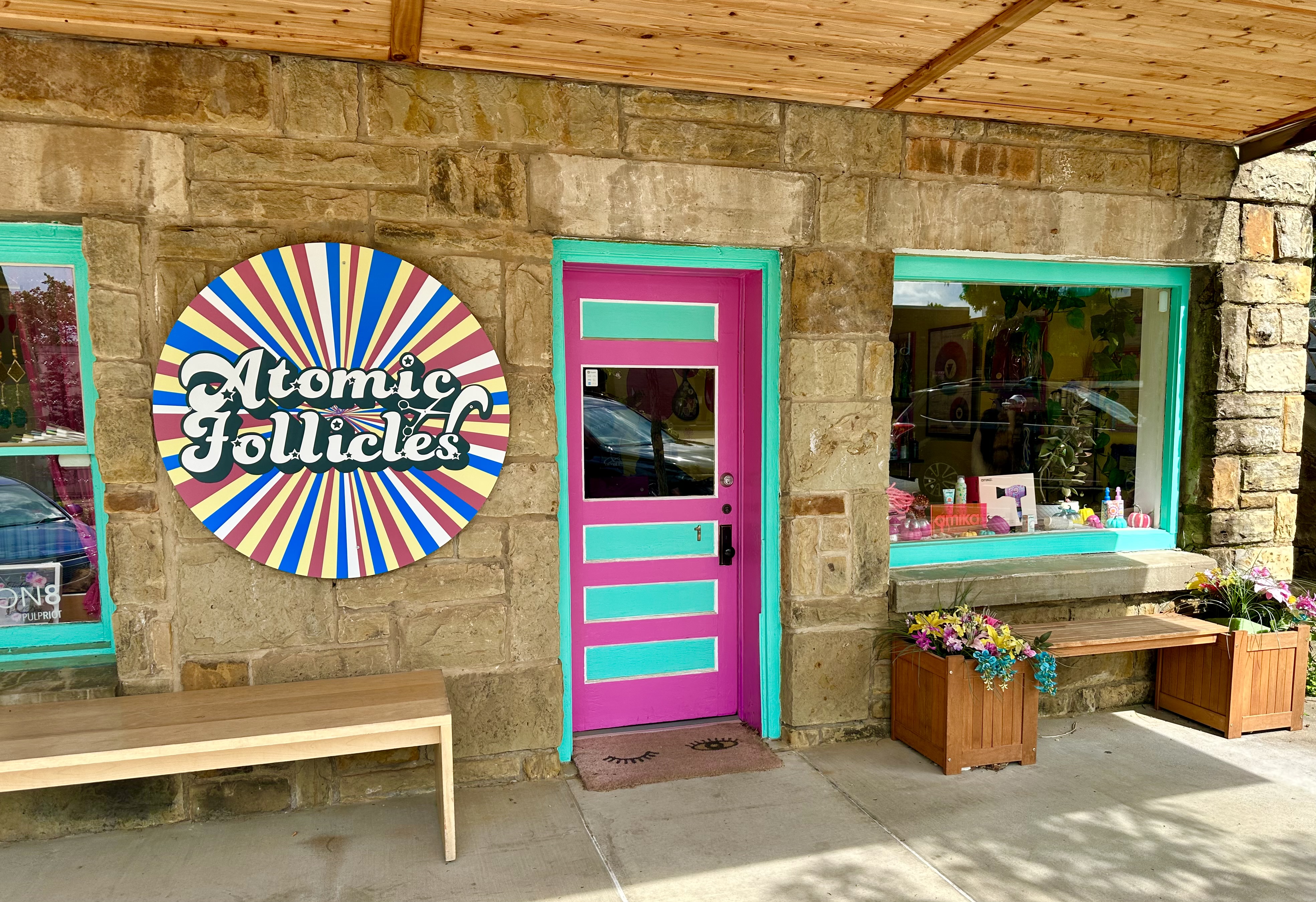 woman with black and pink hair and man with rainbow dreadlocks stand in front of atomic follicles salon