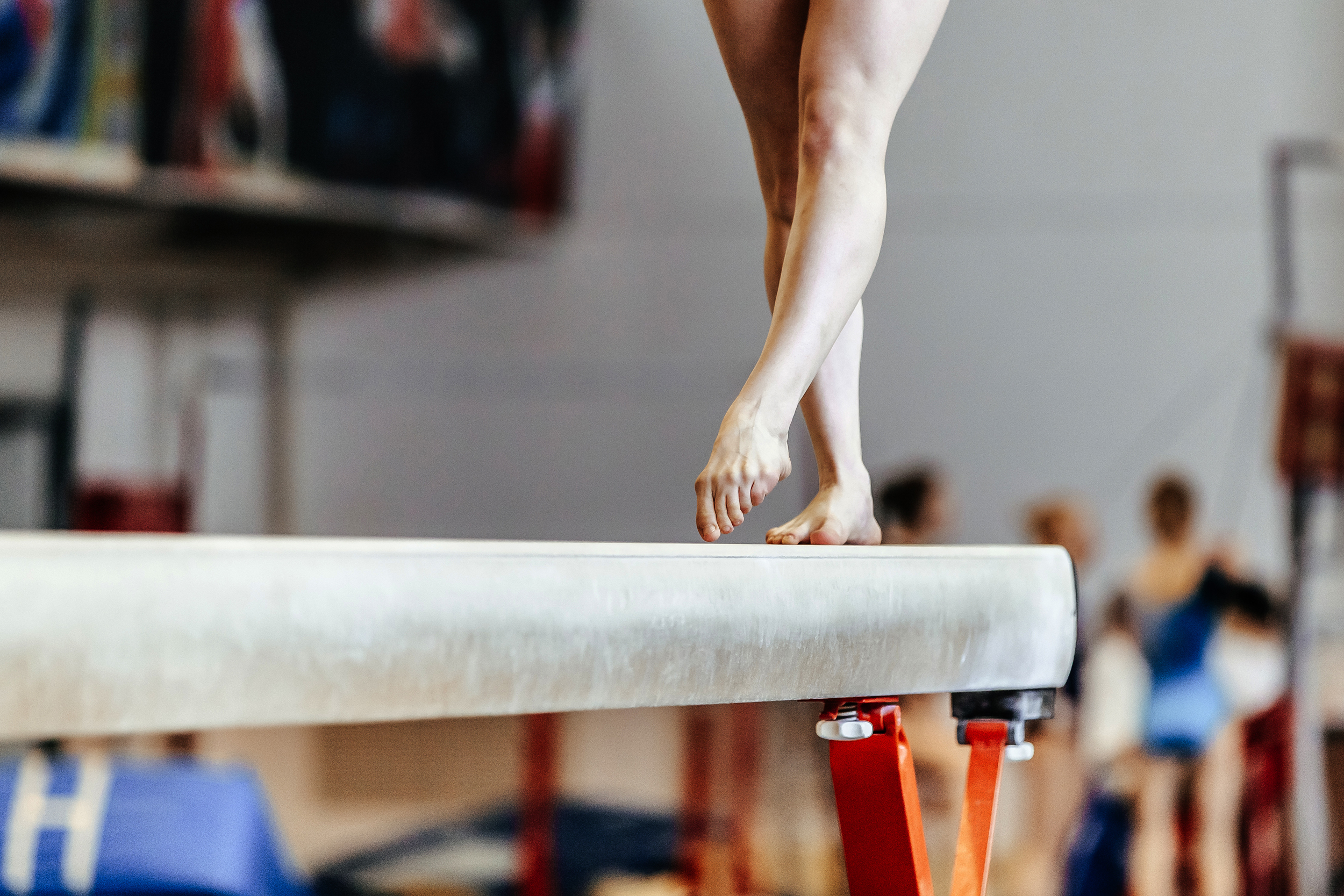 Gymnast's bare feet balancing on a beam, focus on legs and feet.