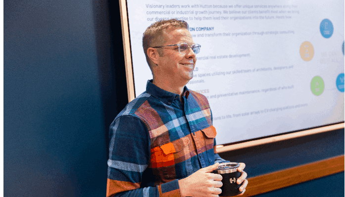 Ben Hutton standing in front of a display screen showing Hutton service offerings.