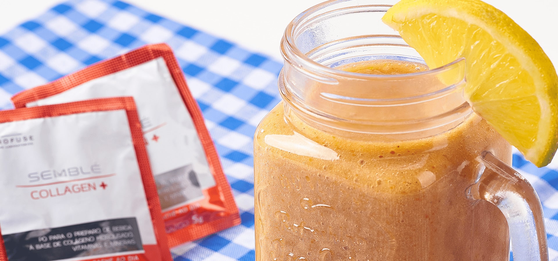 Banner com um sachê de Semblé Collagen+ em cima de uma toalha de mesa xadrez azul e branca junto com um copo de smothie de banana