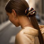 Girl with a long straight ponytail looks down with a striped scrunchie in her hair