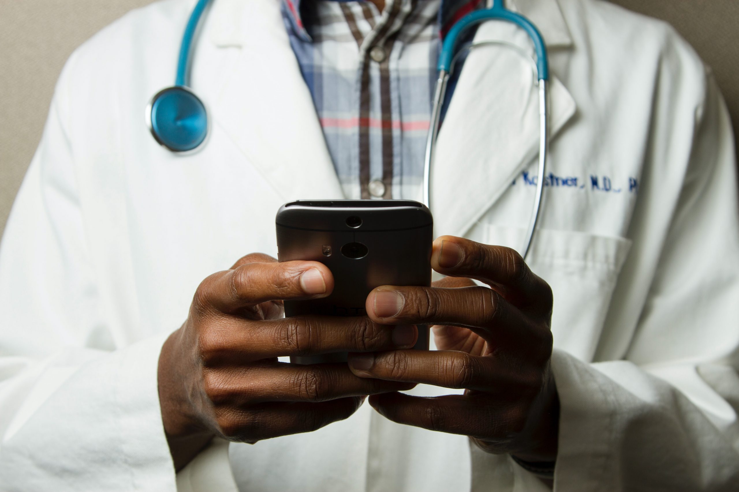 Person in white coat with stethoscope holding cell phone