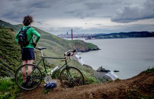 Man standing on cliff with bike looking at the golden gate bridge