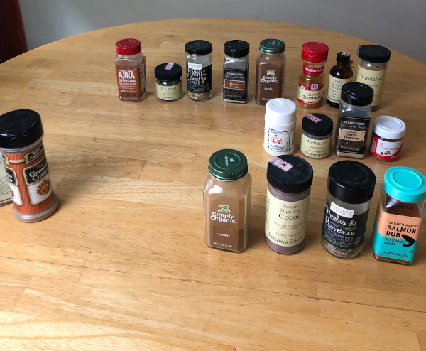 18 spice jars sit on a wooden tabletop.