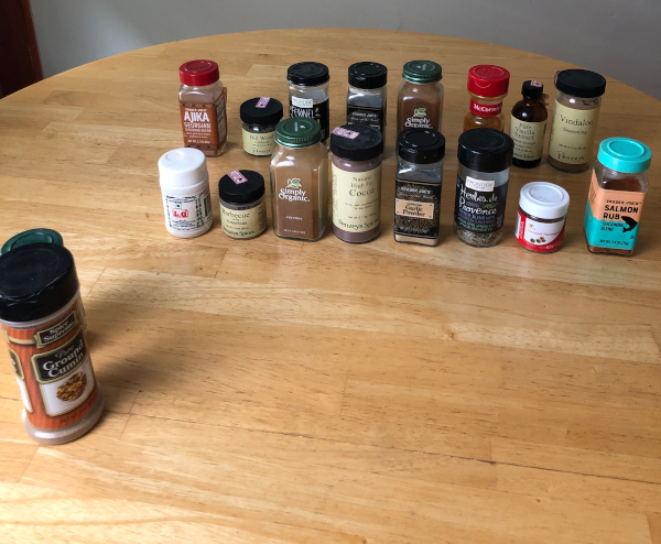 18 spice jars sit on a wooden tabletop.