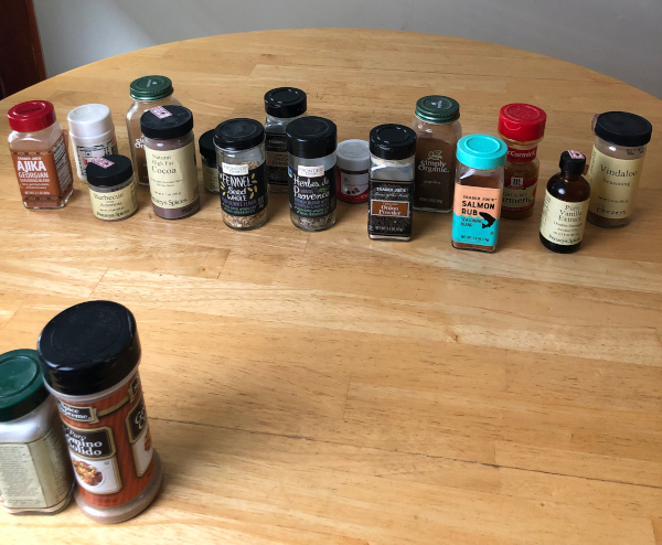 18 spice jars sit on a wooden tabletop.