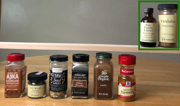 A row of 2 spice jars, outlined in a green rectangle, sit on a wooden shelf. Another 6 spice jars sit below on a wooden countertop.