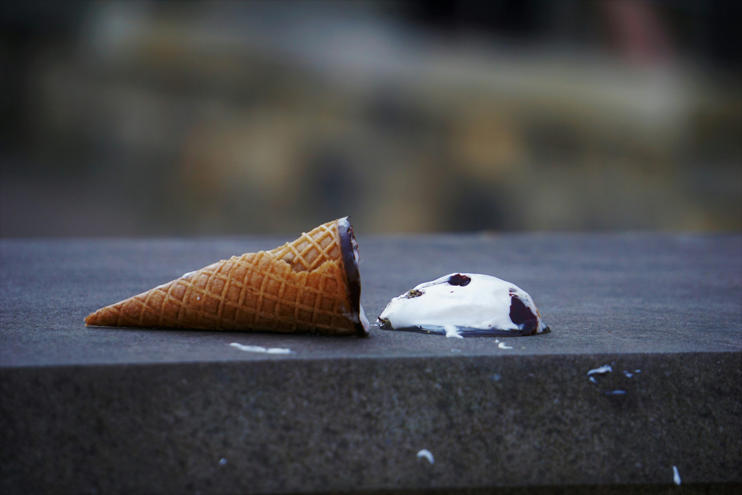 An ice cream lying on its side on pavement. The ice cream lies separate from the cone.