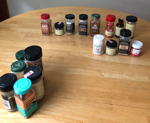 18 spice jars sit on a wooden tabletop.